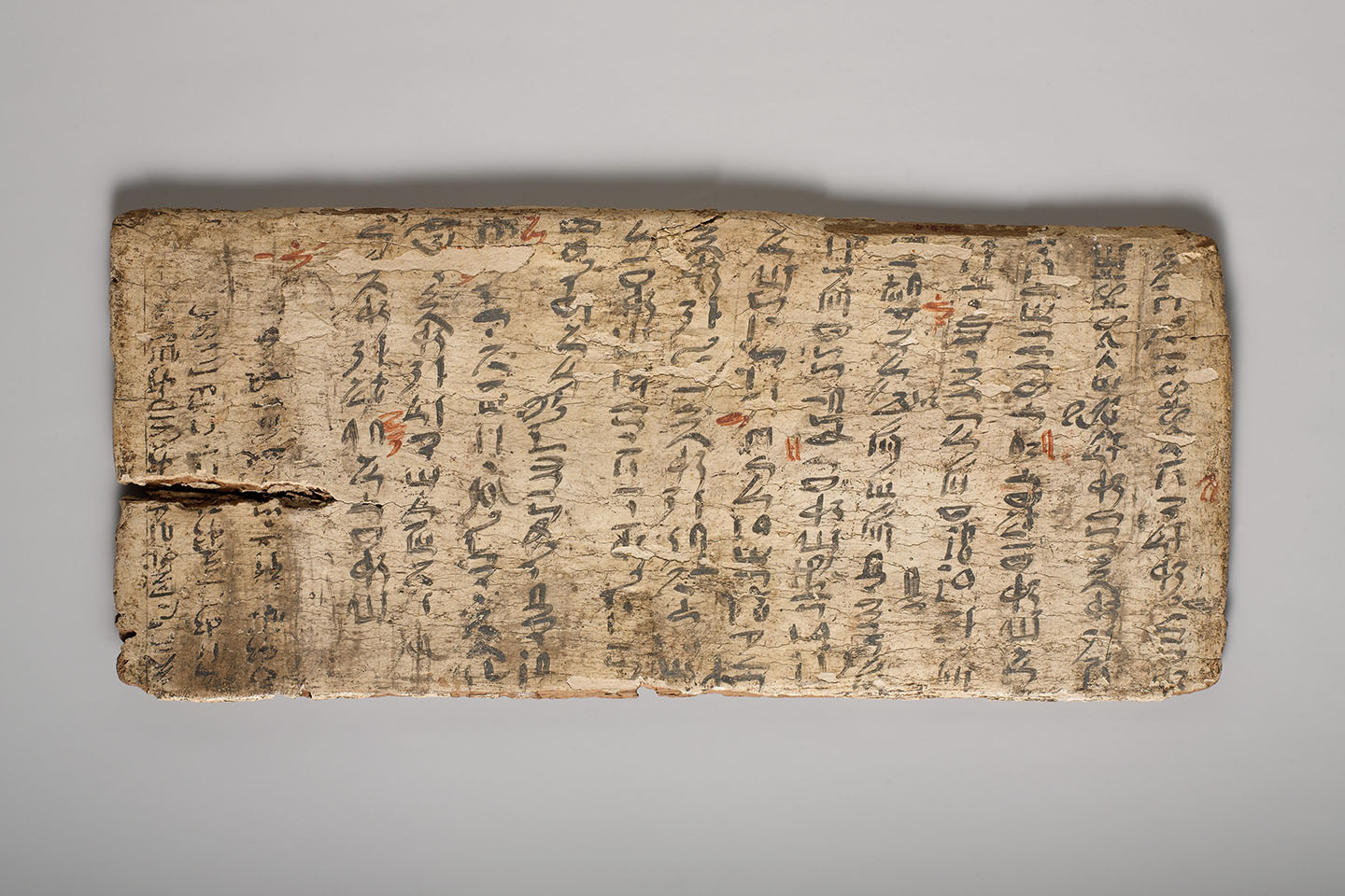 A long rectangular tablet painted mostly with black and some red calligraphic characters in consecutive vertical columns spanning the full width of the tablet